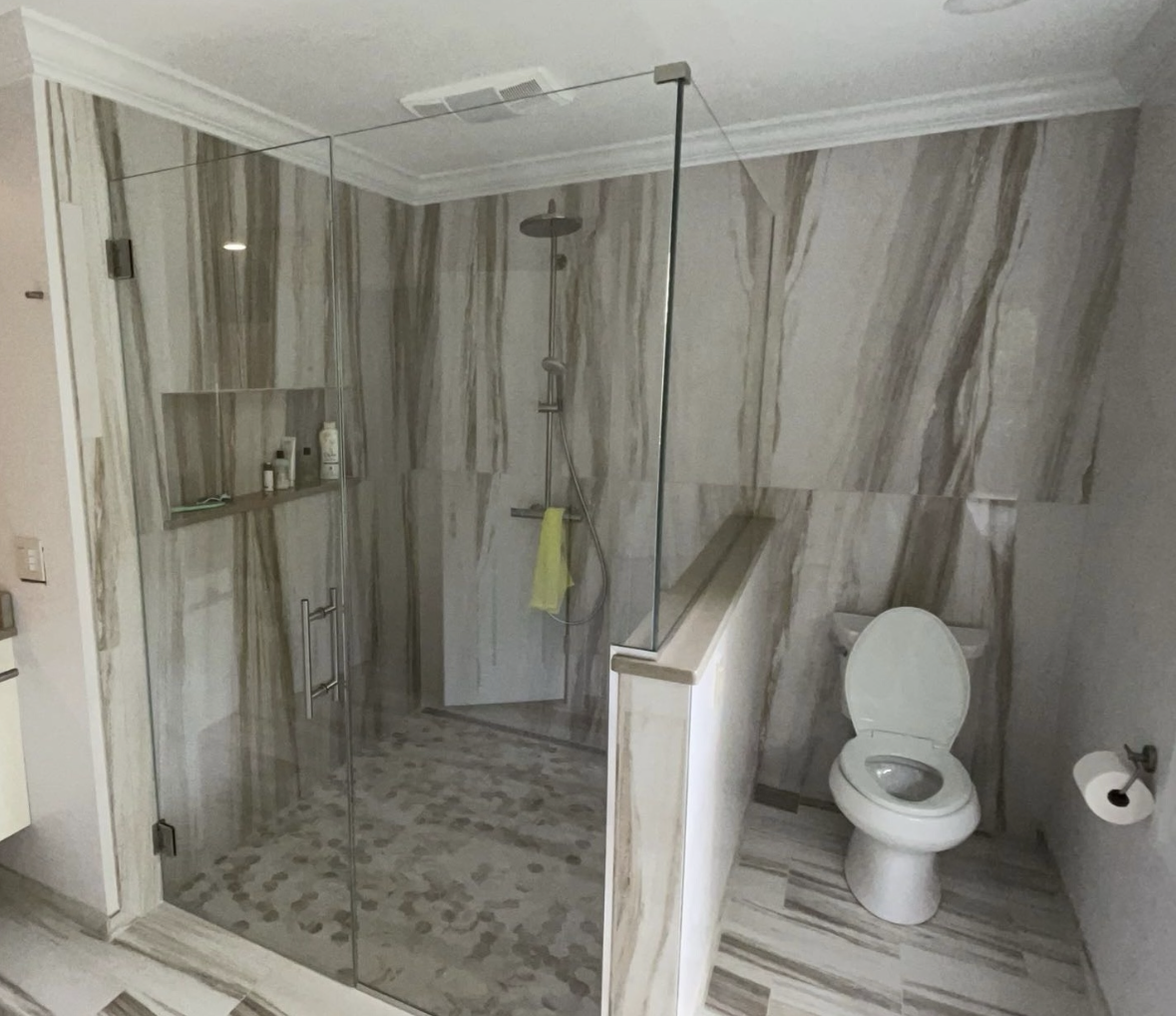Modern bathroom with marble-patterned walls and floors, featuring a glass-enclosed walk-in shower and a toilet with the seat up.