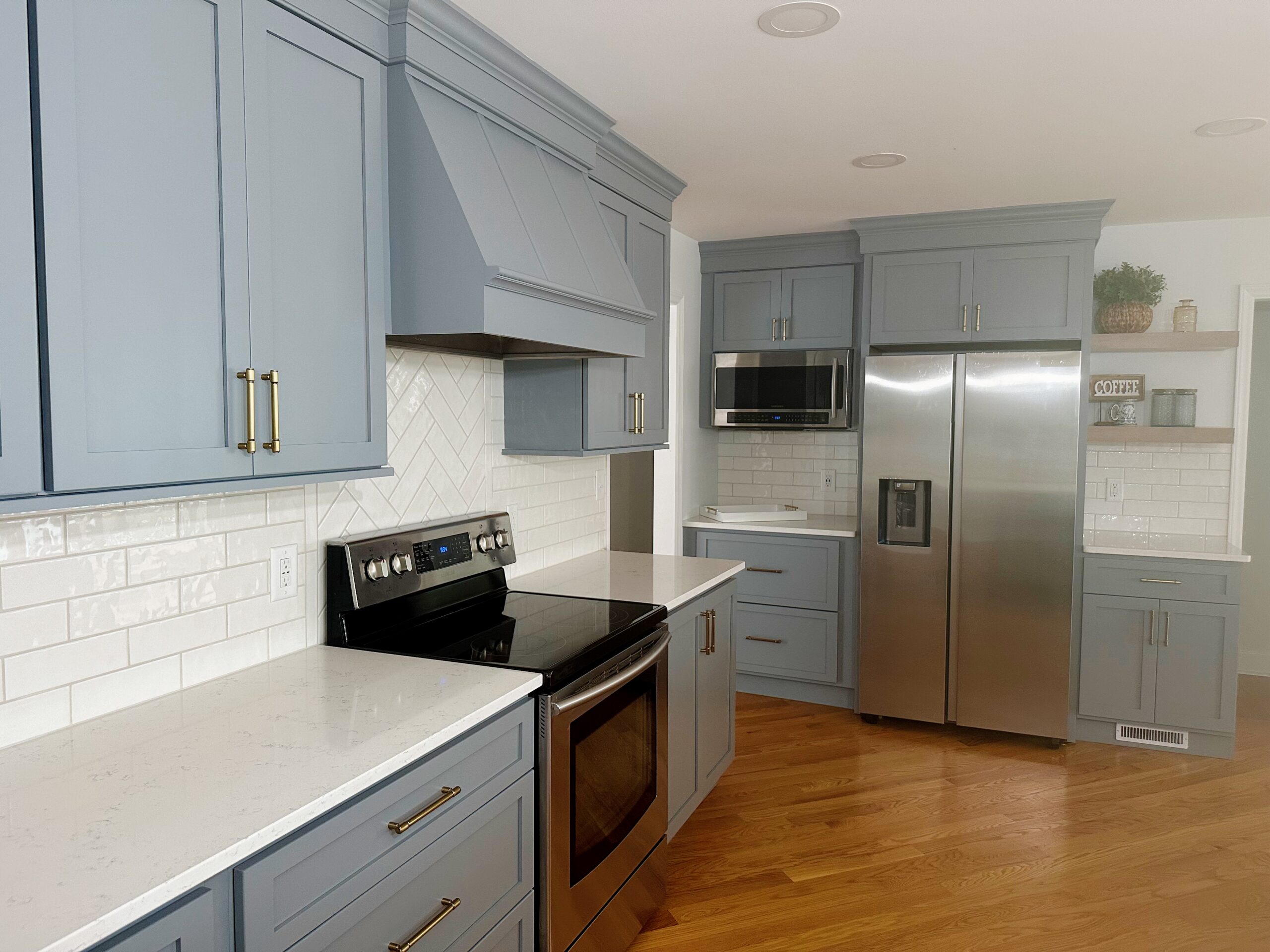 Modern kitchen with blue cabinets, stainless steel appliances, white countertops, subway tile backsplash, and wooden floor.